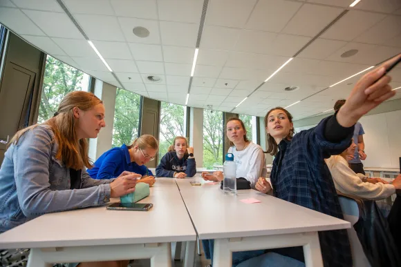 Middelbare scholieren in een klaslokaal. Eén scholier wijst enthousiast naar iets in de verte.