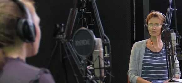 Two women wearing headphones and sitting at a microphone