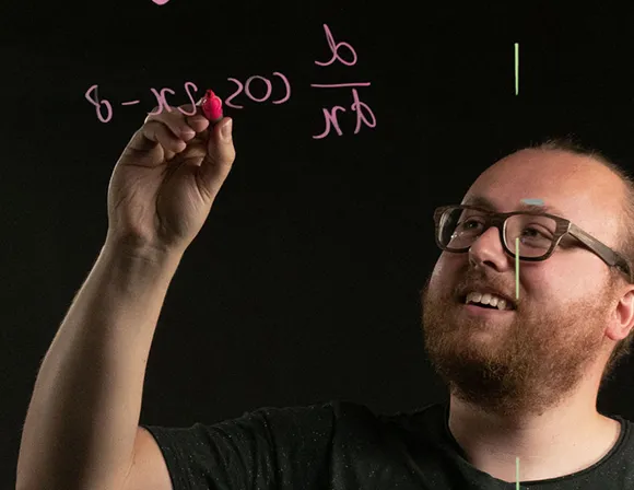 Man with beard and glasses writing on a lightboard.