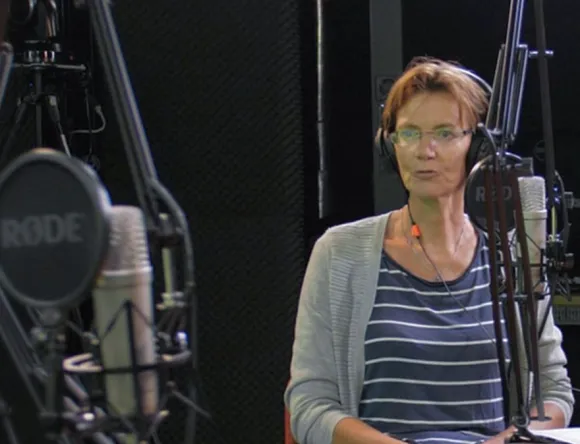 Two women wearing headphones and sitting at a microphone