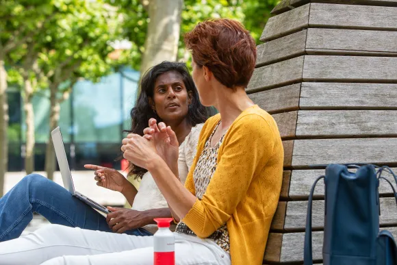 Twee vrouwen zitten buiten op de campus te overleggen