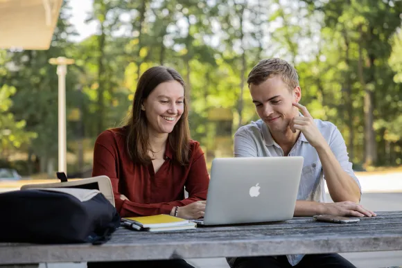 Twee studenten werken samen achter een laptop in de buitenlucht