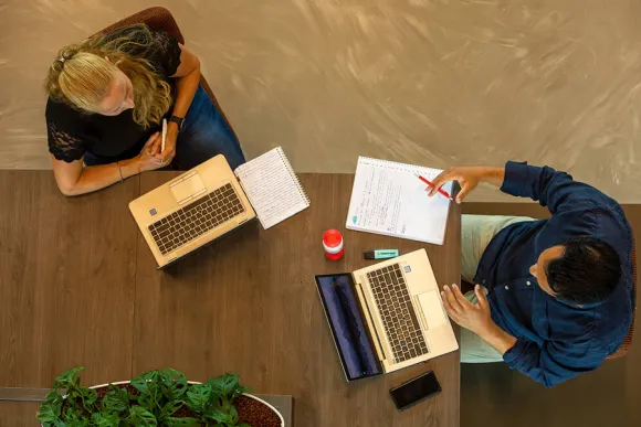 Twee medewerkers overleggen met hun laptop en papier