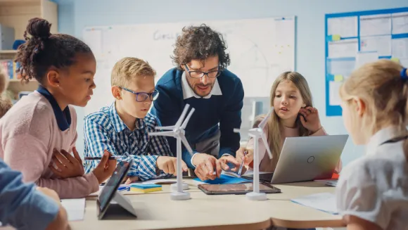 Basisschool klaslokaal: enthousiaste leraar met tabletcomputer legt aan briljante jonge kinderen uit hoe windturbines werken.