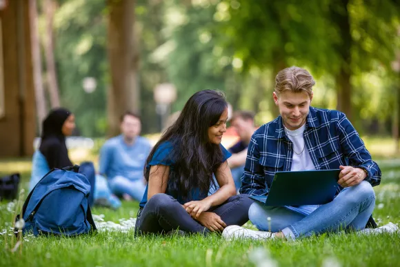 Twee studenten buiten in het gras, allebei kijkend naar een laptop.