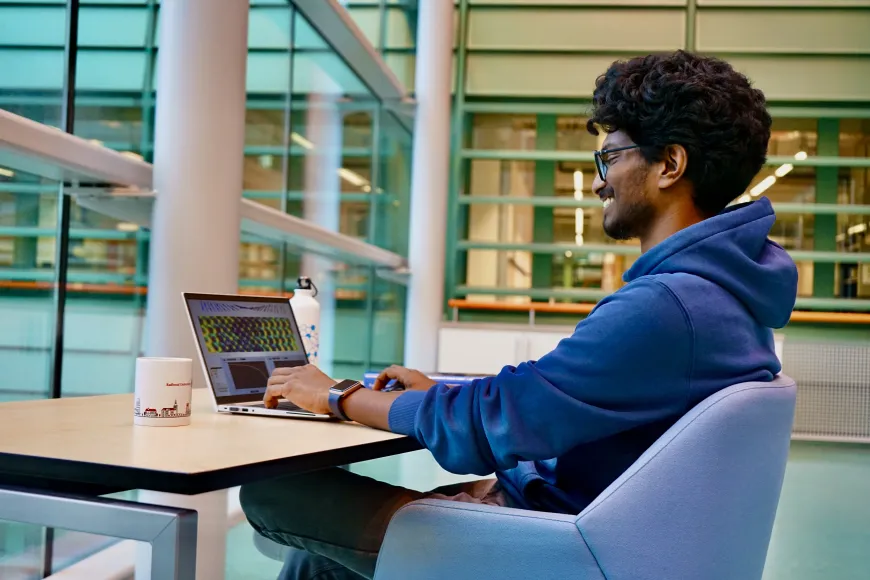 Nikhil Seeja Sivakumar zit achter een laptop te werken in het Huygensgebouw.