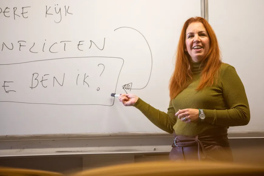 Barbara van Riel, een witte vrouw met oranje haar, legt iets uit voor een whiteboard.