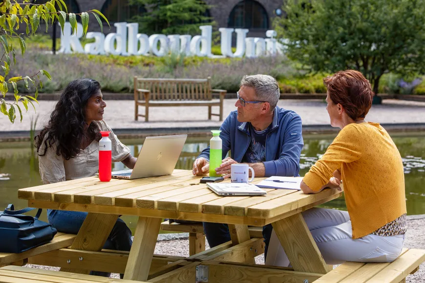 Drie medewerkers overleggen buiten aan een picknicktafel