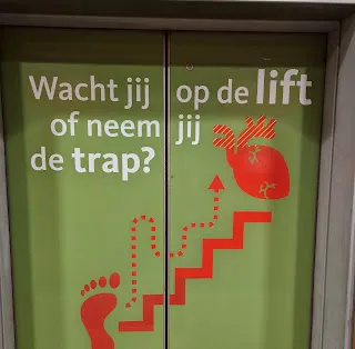 Liftdeur met opschrift 'Wacht jij op de lift of neem jij de trap?'
