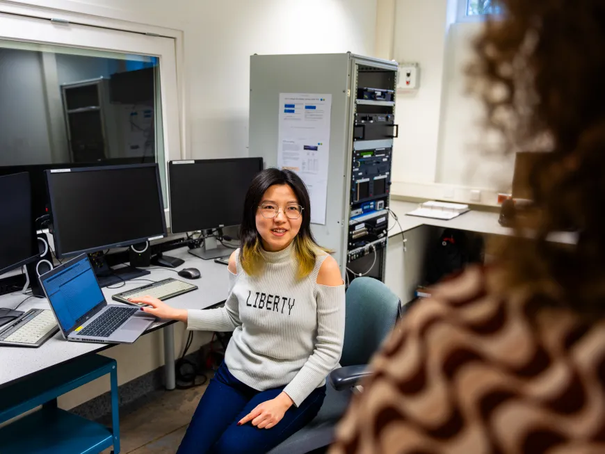 Een foto van Yuxuan Dai aan het werk achter een laptop terwijl ze met iemand praat.