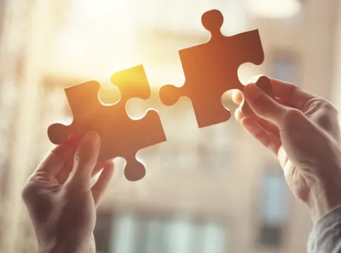 Hands holding two pieces of a puzzles.