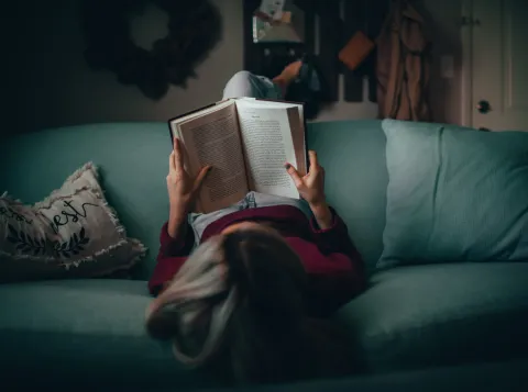 Person is laying on the sofa and reading a boko