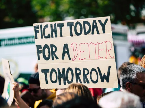 A picture showing a protest. A board is held up that says: fight today for a better tomorrow 