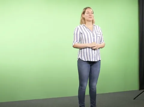Een vrouw in een streepjesblouse die voor een greenscreen staat.