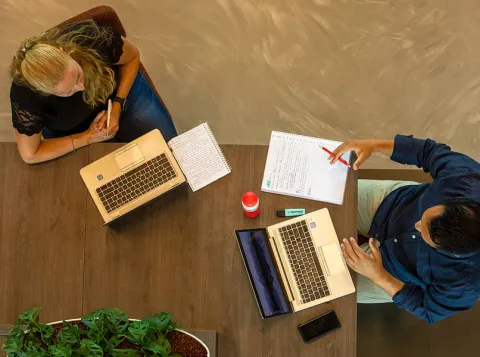 Twee medewerkers overleggen met hun laptop en papier