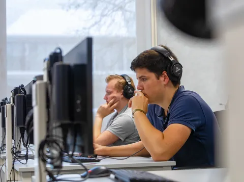 Een student met een koptelefoon op achter een computer in het Comeniusgebouw.