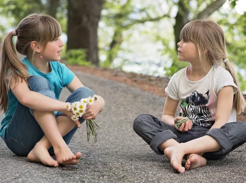 Two children talking to each other sitting on the ground