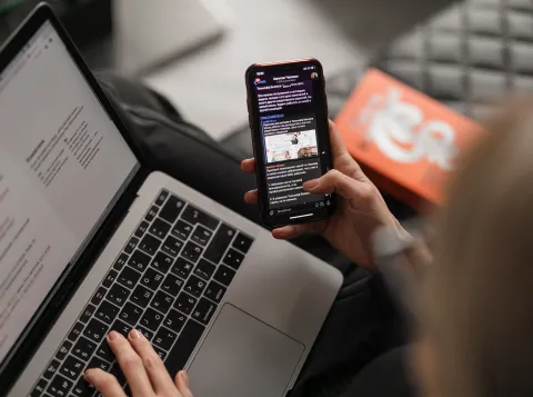 A person looking at their phone and laptop.