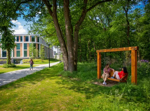 Een foto van twee studenten op een schommelbank met het Maria Montesorrigebouw in de achtergrond.