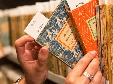 Een closeup foto van een persoon die twee boeken uit een boekenkast pakt. Alleen de handen en de boekenkast zijn zichtbaar.