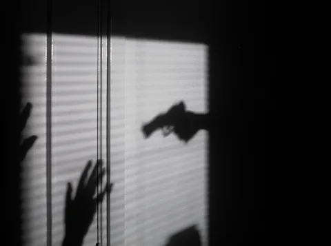 Shadow on wall with gun and hands in the air.