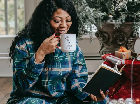 Smiling black woman reading book and drinking hot coffee by Any Lane, Pexels