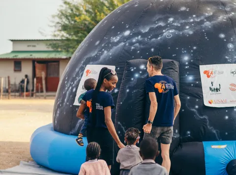 Kleuters gaan met het AMT team het mobiele planetarium binnen in Okaukuejo, Namibië