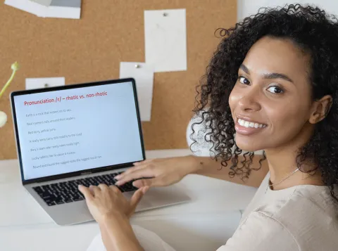Vrouw kijkt in de camera terwijl ze achter een laptop zit