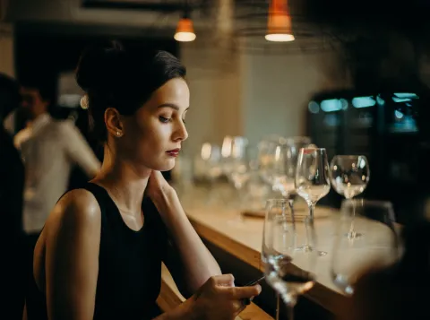 Alleenstaande vrouw aan de bar met haar mobiel in de hand