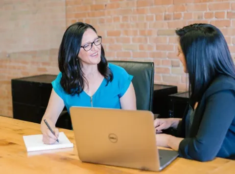 Twee vrouwen praten met elkaar aan een bureau