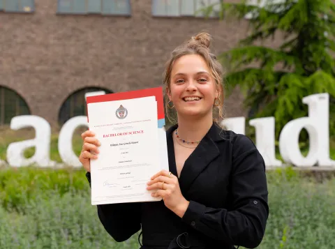 Student Suus volgde extra vakken over duurzaamheid en behaalde een duurzaamheidsgetuigenis op haar bachelordiploma. Ze poseert trots met haar diploma.