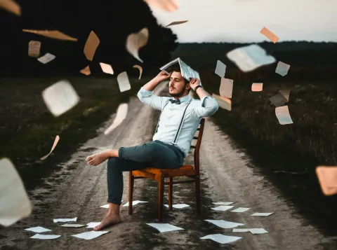 Man zit in een veld op een stoel met een boek boven zijn hoofd