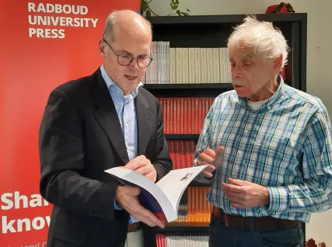 🎓Frans Keune (rechts op de foto) presenteert trots zijn boek aan Prof. Dr. T.M. Heskes vice-decaan Radboud Faculteit der Natuurwetenschappen, Wiskunde en Informatica (foto links).