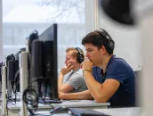 Een student met een koptelefoon op achter een computer in het Comeniusgebouw.