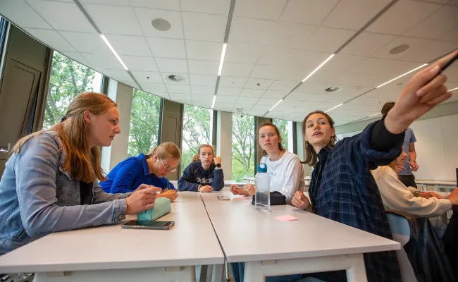 Middelbare scholieren in een klaslokaal. Eén scholier wijst enthousiast naar iets in de verte.
