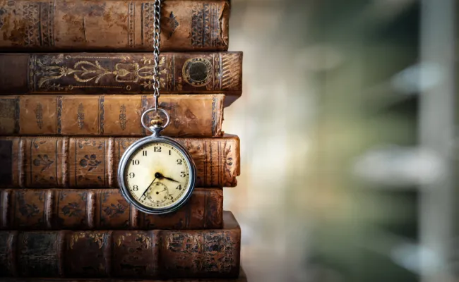 Vintage klok hangend aan een ketting op de achtergrond van oude boeken. Oud horloge als symbool van het verstrijken van de tijd. Concept over het thema geschiedenis, nostalgie, ouderdom.