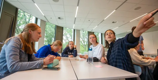 Middelbare scholieren in een klaslokaal. Eén scholier wijst enthousiast naar iets in de verte.