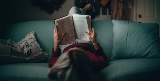 Person is laying on the sofa and reading a boko