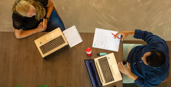 Twee medewerkers overleggen met hun laptop en papier