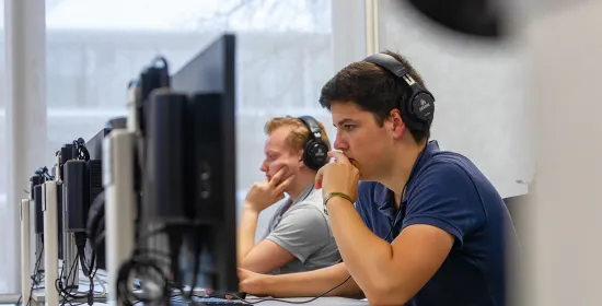Een student met een koptelefoon op achter een computer in het Comeniusgebouw.