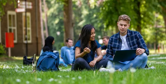 Studenten zitten met hun laptop in het gras op de campus van de Radboud Universiteit