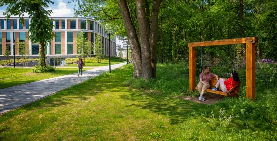 Een foto van twee studenten op een schommelbank met het Maria Montesorrigebouw in de achtergrond.