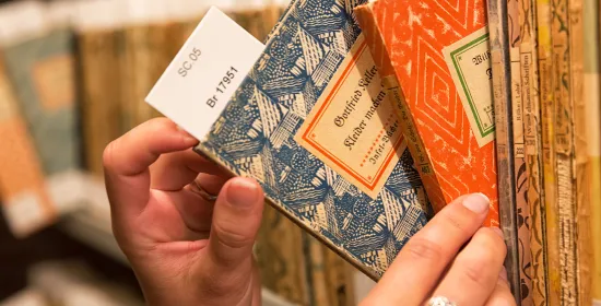 Een closeup foto van een persoon die twee boeken uit een boekenkast pakt. Alleen de handen en de boekenkast zijn zichtbaar.