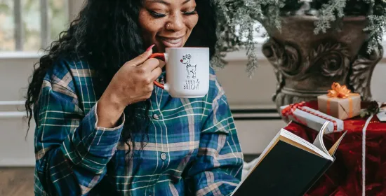 Smiling black woman reading book and drinking hot coffee by Any Lane, Pexels