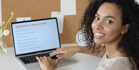 Vrouw kijkt in de camera terwijl ze achter een laptop zit