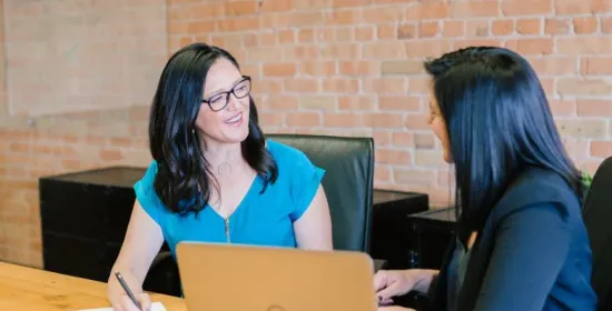 Twee vrouwen praten met elkaar aan een bureau