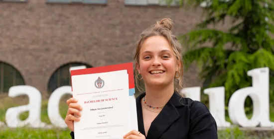 Student Suus volgde extra vakken over duurzaamheid en behaalde een duurzaamheidsgetuigenis op haar bachelordiploma. Ze poseert trots met haar diploma.