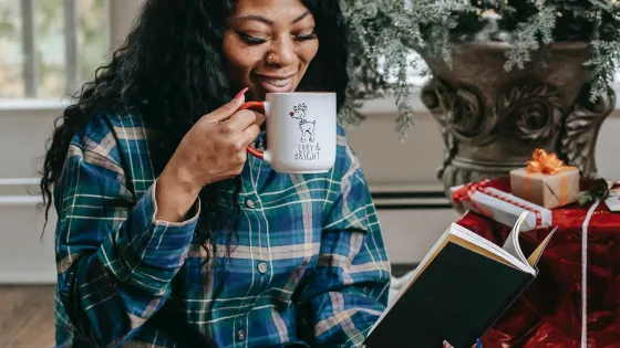 Smiling black woman reading book and drinking hot coffee by Any Lane, Pexels